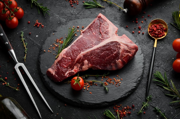 Raw T-bone steak on a stone table with thyme, rosemary and spices. Top view. Flat lay top view on black stone cutting table.