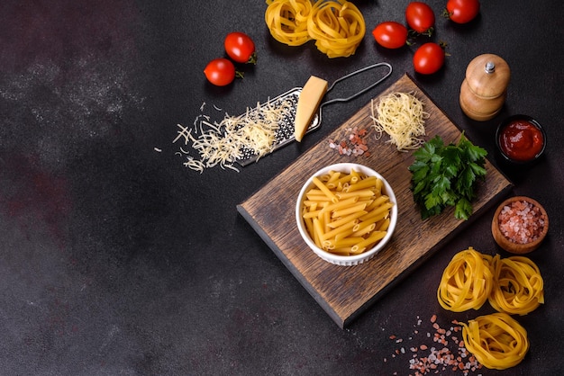 Raw tagliatelle paste with grated cheese cherry tomatoes spices and herbs on a wooden cutting board