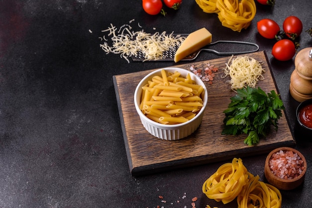 Raw tagliatelle paste with grated cheese cherry tomatoes spices and herbs on a wooden cutting board