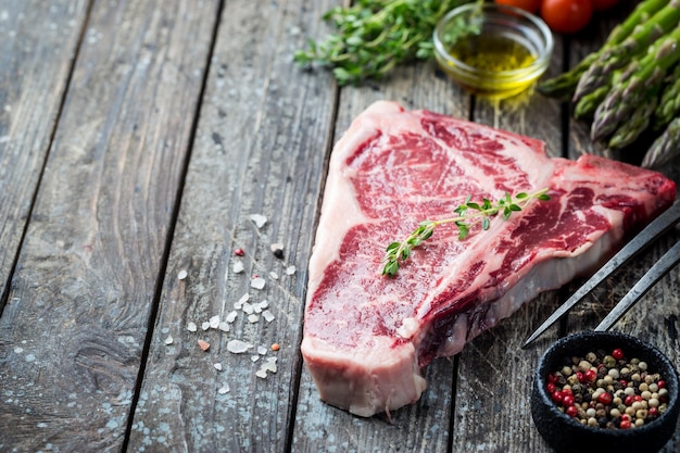 Photo raw tbone steak with fresh herbs and oil on dark wooden background