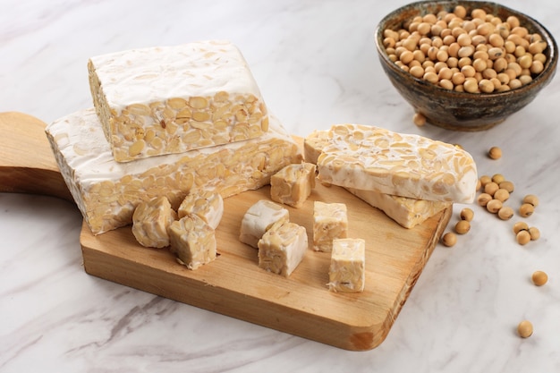 Raw Tempeh or Tempe. Tempeh Slices on Wooden Background, Cut with Knife on Wooden Board WHite Background. Tempe Made From Fermented Soybeans