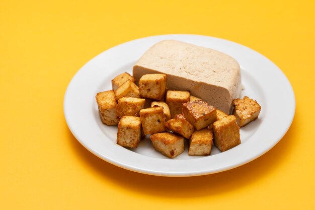 Raw tofu block on white small dish on yellow