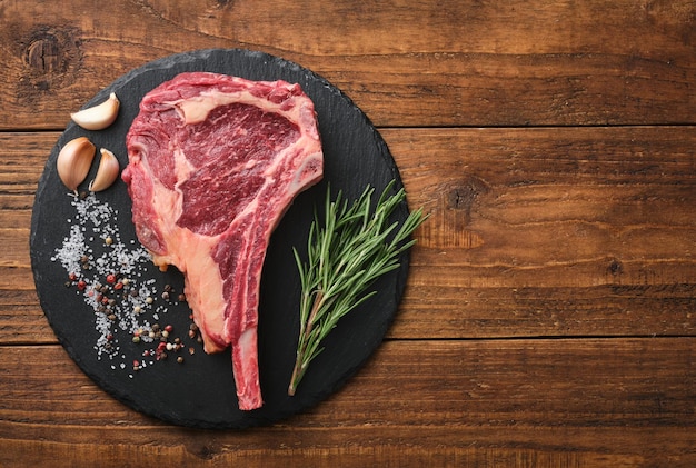 Raw tomahawk beef steak with ingredients for grilling rosemary salt pepper and garlic