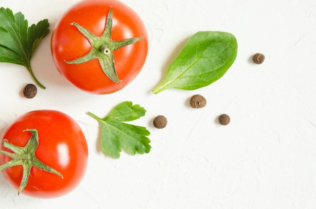 Raw tomatoes, herbs and black pepper on a light concrete background