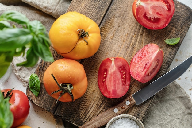 Raw tomatoes and knife on wooden board surrounded by ingredients Top view