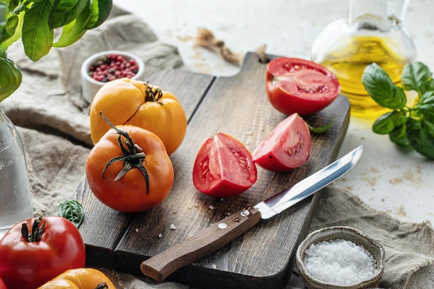 Raw tomatoes  on wooden cutting board surrounded by ingredients Rustic cooking background