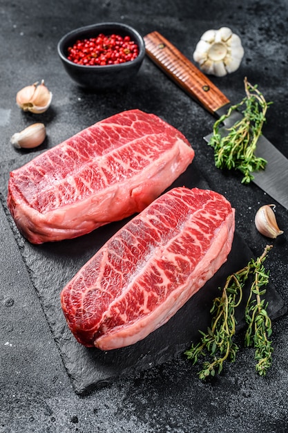 Raw top blade steak dry-aged on a stone board on black. Top view.