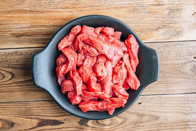 Raw uncooked beef meat sliced in strips with Ingredients for beef stroganoff over rustic wooden background