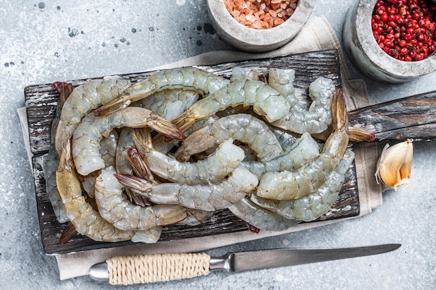 Raw uncooked black Headless shrimps prawns on a wooden Board. Gray background. Top view.