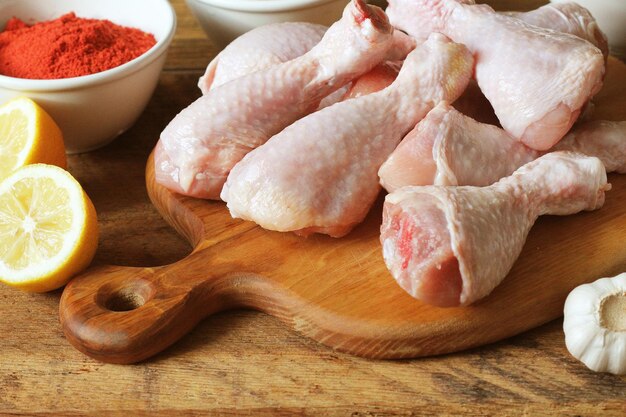 Photo raw uncooked chicken legs drumsticks on cutting board meat with ingredients for cooking