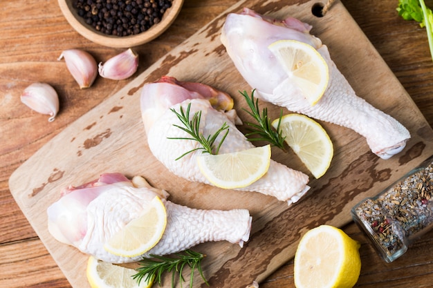 Raw uncooked chicken legs, drumsticks on wooden board, meat with ingredients for cooking