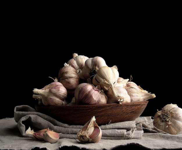 Raw unpeeled garlic in a brown ceramic plate on a gray linen napkin