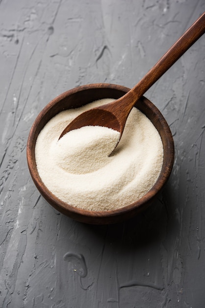 Raw unprepared semolina flour also known as Rava powder in Hindi in bowl or spoon. close-up isolated on white or moody background. selective focus