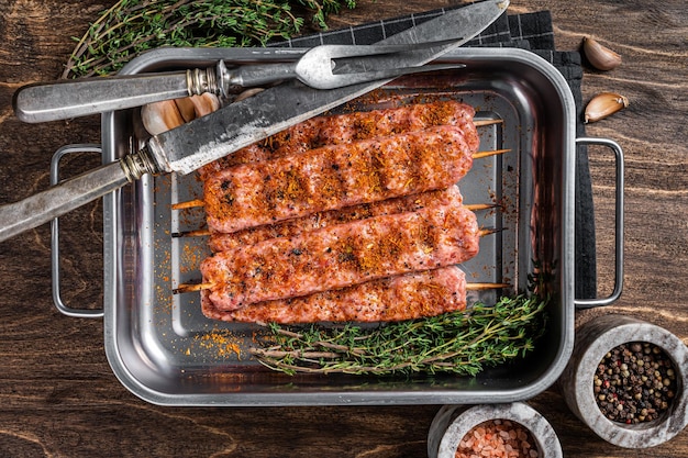 Raw Urfa shish kebab in butcher tray with herbs Wooden background top view