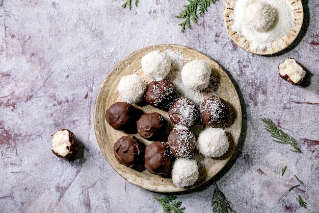 Raw vegan homemade coconut chocolate candy balls with coconut flakes in ceramic plate over white wooden background