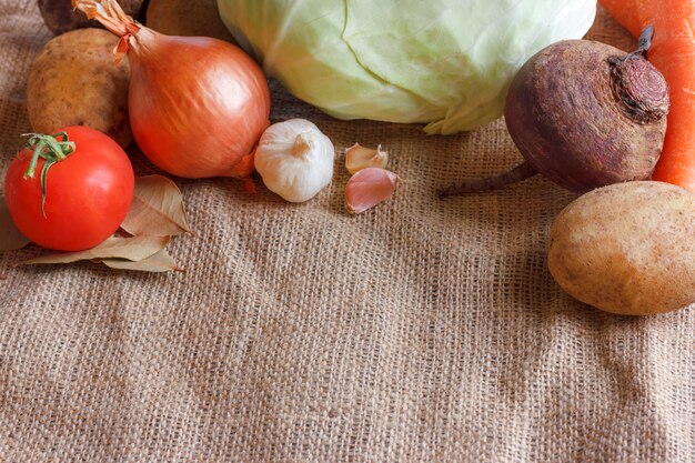 Raw vegetables for beet soup borscht. White cabbage, beet, carrot, potato, tomato, garlic on a wooden board