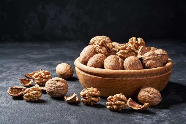 Raw walnut in wooden bowl on black , close-up.