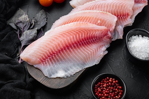 Raw white fish tilapia, with basmati rice and cherry tomatoes ingredients, on black table