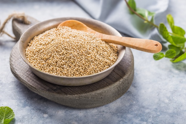 Raw white quinoa seeds on plate with wooden spoon