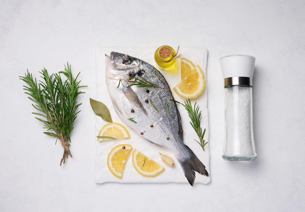 Raw whole dorado fish on white board and spices for cooking top view on white table