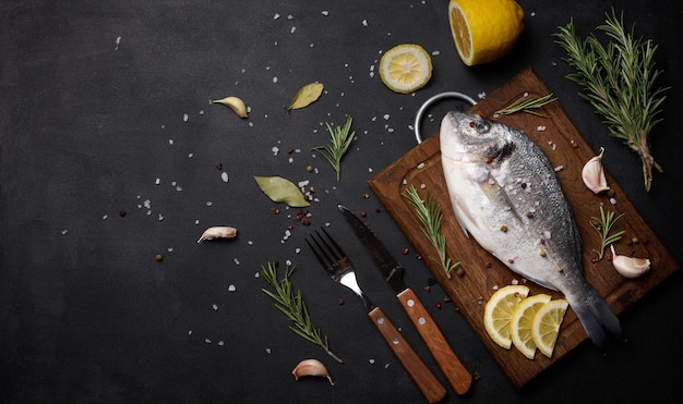 Raw whole dorado fish on wooden kitchen board and spices for cooking top view on black table