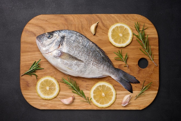 Raw whole dorado fish on wooden kitchen board and spices for cooking top view on black table