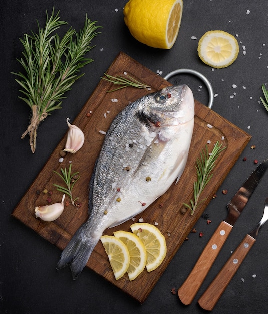 Raw whole dorado fish on wooden kitchen board and spices for cooking top view on black table