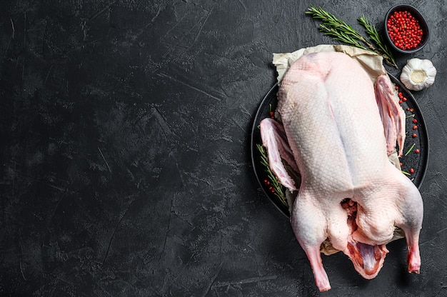 Raw whole duck, pink pepper and rosemary. Black background. Top view. Space for text