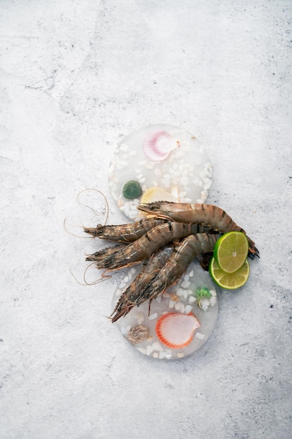 Raw whole fresh uncooked prawns shrimps on decorated ice with lime on gray stone background