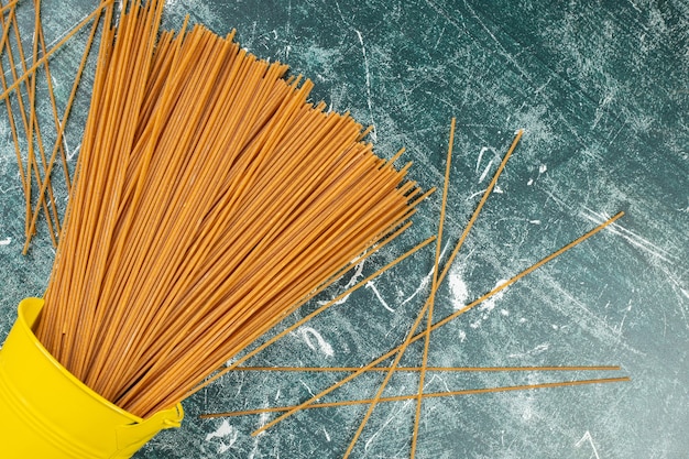 Raw whole grain pasta spaghetti in a overturned bucket , on the blue.