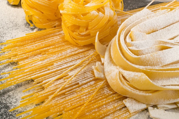 Raw yellow italian pasta pappardelle, fettuccine or tagliatelle close up. Egg homemade noodles cooking process, long rolled macaroni or uncooked spaghetti