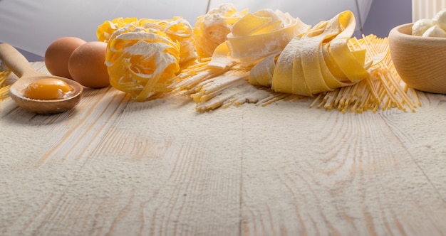 Photo raw yellow italian pasta pappardelle, fettuccine or tagliatelle close up with eggs. egg homemade noodles cooking process with long macaroni or spaghetti