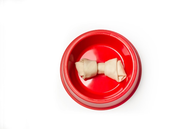 A rawhide bone in a red pet bowl on a white background