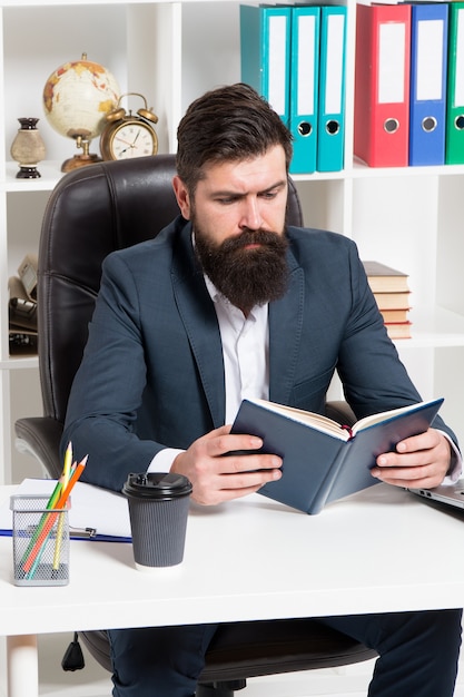 Reading authority business book. Man bearded hipster boss sit armchair office interior read book. Boss at workplace. Guy formal clothing corporate style working. Business literature. Boss read book.