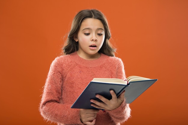 Reading practice for kids Childrens literature Girl hold book read story over orange background Child enjoy reading book Book store concept Wonderful free childrens books available to read