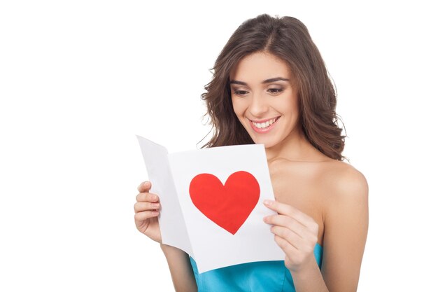 Reading a Valentine card. Attractive young woman reading a valentine card while standing isolated on white background