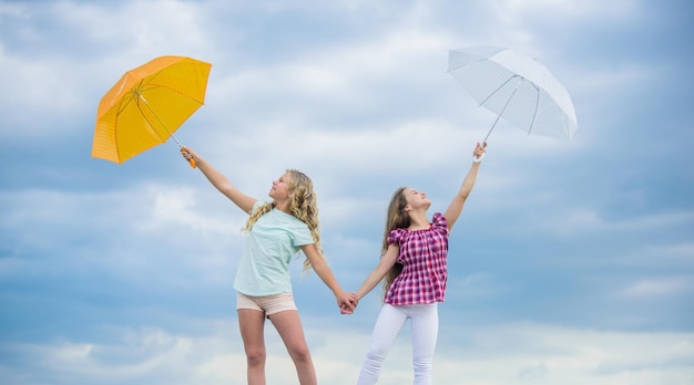 Ready for any weather Girls friends with umbrellas cloudy sky background Weather forecast Weather changing Carefree children outdoors Windy or rainy we are prepared Freedom and freshness