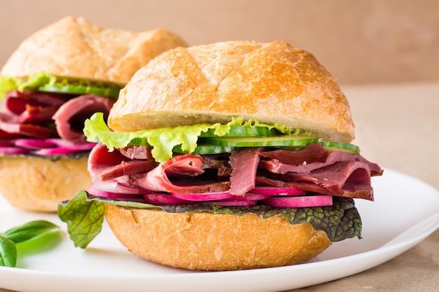 Ready-to-eat hamburger with pastrami, vegetables and basil on a plate on craft paper. American fast food. Close-up