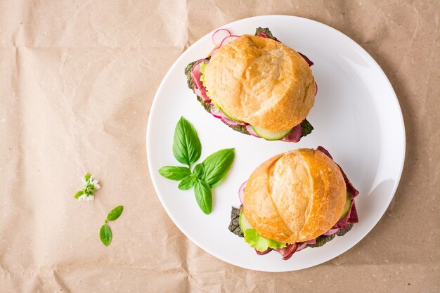 Ready-to-eat hamburgers with pastrami, vegetables and basil on a plate on craft paper. American fast food. Top view