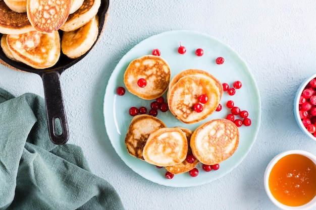 Ready to eat pancakes and cranberries on a plate and a bowl of honey on the table Homemade breakfast dessert Top view