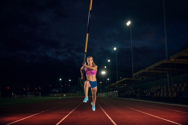 Ready to overcome difficulties. Professional female pole vaulter training at the stadium in the evening. Practicing outdoors. Concept of sport, activity, healthy lifestyle, action, movement, motion.