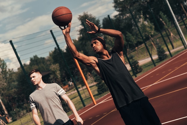 Ready to shoot. Two young men in sports clothing playing basketball while spending time outdoors