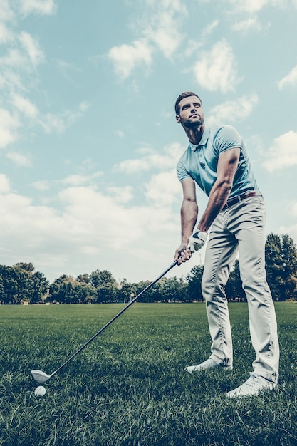 Photo ready to strike. low angle view of young man playing golf while standing on green