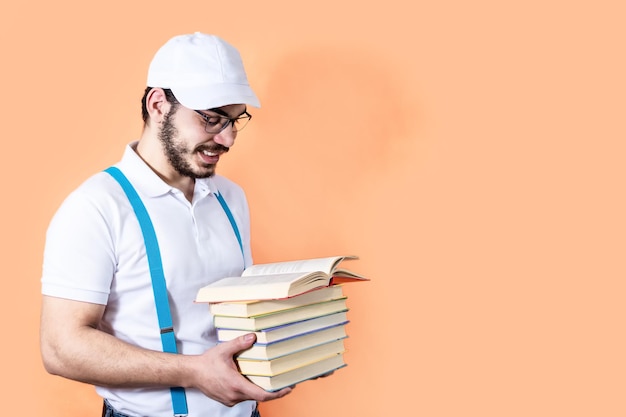 Ready to study hard Young man holding a stack of books on a light orange background