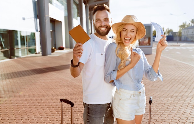 Photo ready for vacation excited spouses with suitcases showing boarding passes and passports standing