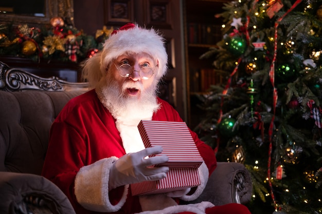 Real authentic surprised Santa Claus holds Christmas gift. Fulfillment of desires. Santa sitting at