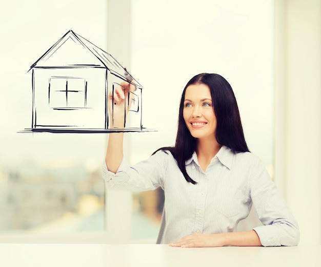 real estate, accomodation and technology concept - smiling woman drawing house on virtual screen