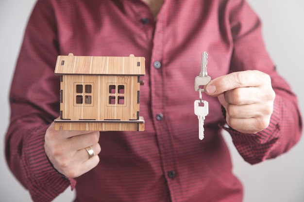 Real estate agent holding house keys with a house model in office Business concept