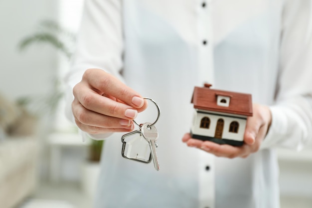 Real estate agent holding house model and key indoors closeup