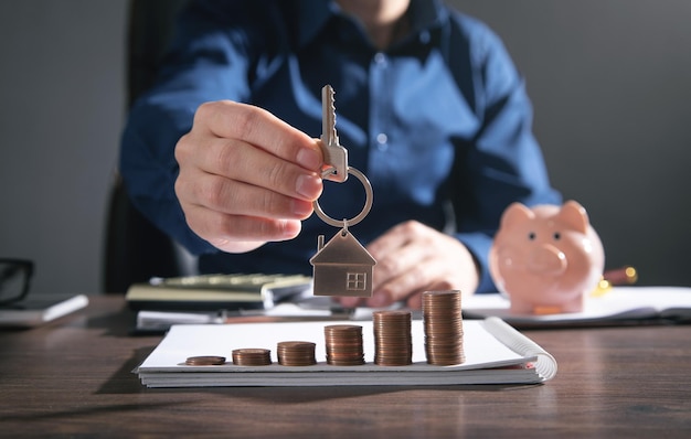 Real estate agent showing house key over stack of coins.